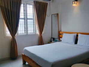 A hotel room with a bed, curtains, a bedside table, a mirror, and a wall-mounted light fixture. - Prime Legacy (Bengaluru)