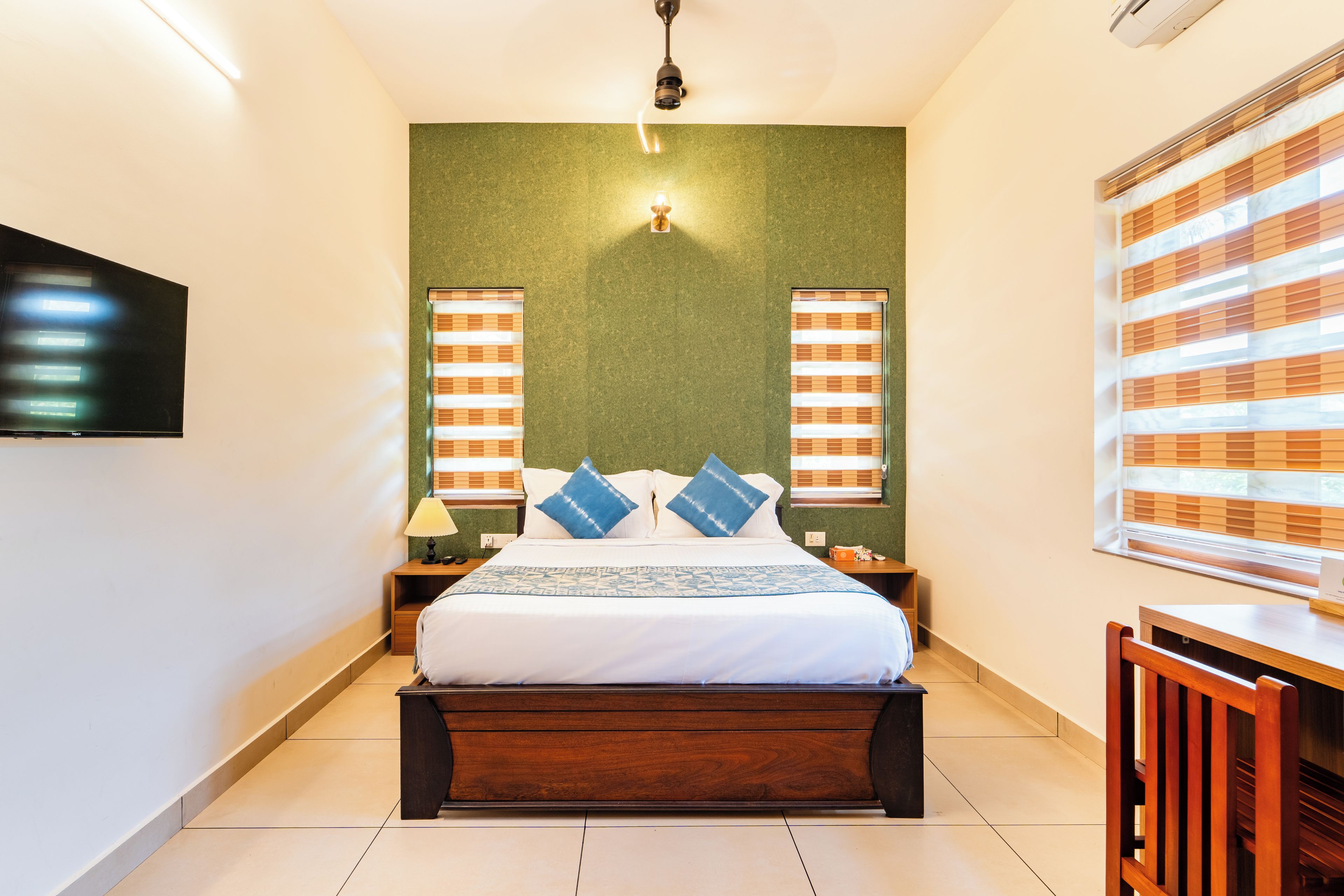 A hotel room with a bed, bedside tables, a desk, and a television.