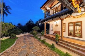 A two-story building with a balcony, a stone pathway leading to the entrance, and a well-maintained garden. - ELIVAAS Signature Pochans Zen 3BHK Villa (Thattekad)