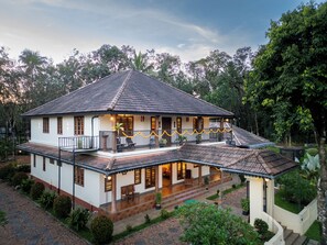 A two-story house with a balcony, surrounded by greenery.
