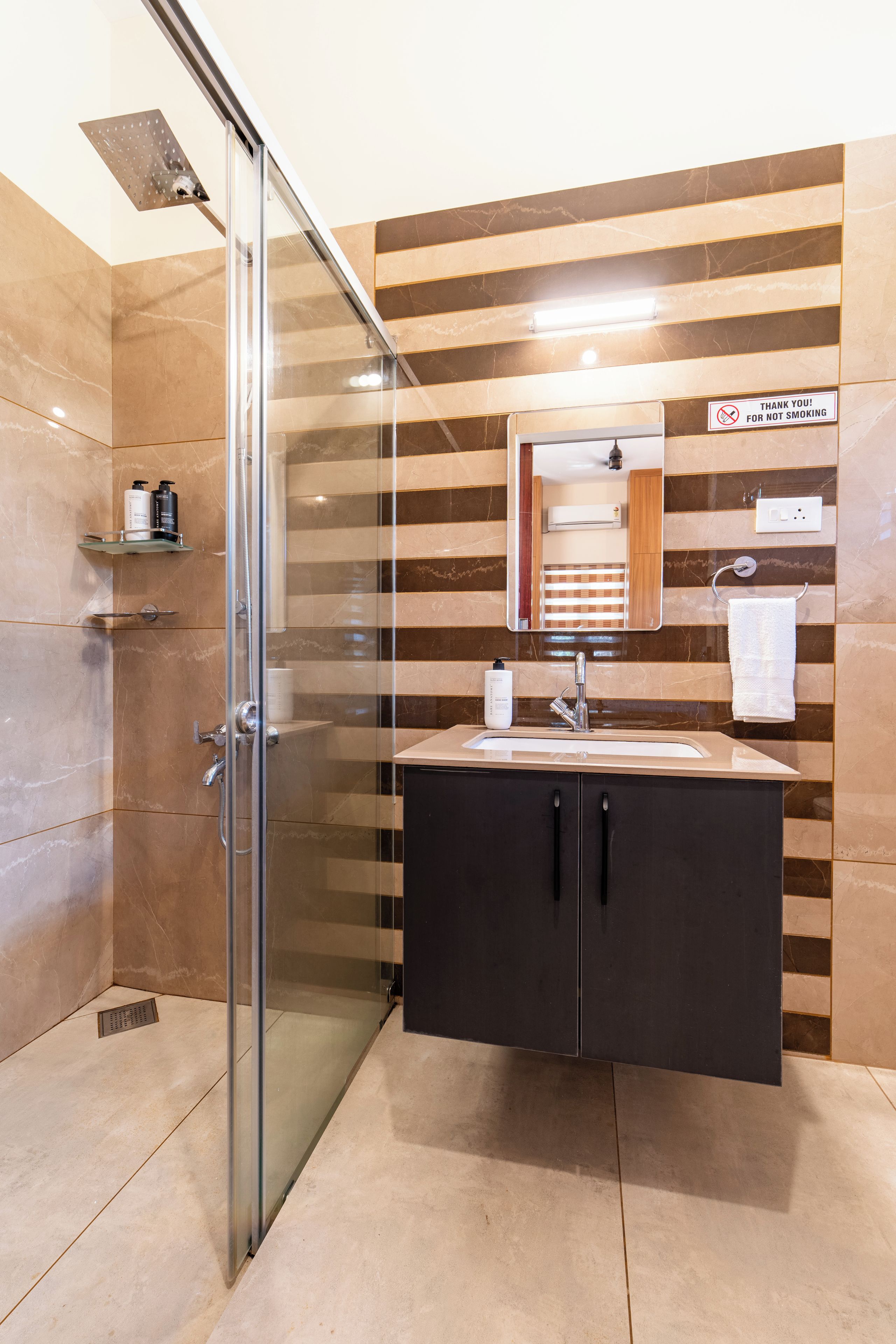 A modern bathroom with a glass shower enclosure, a vanity with a mirror, and a 'Thank you! For not smoking' sign.