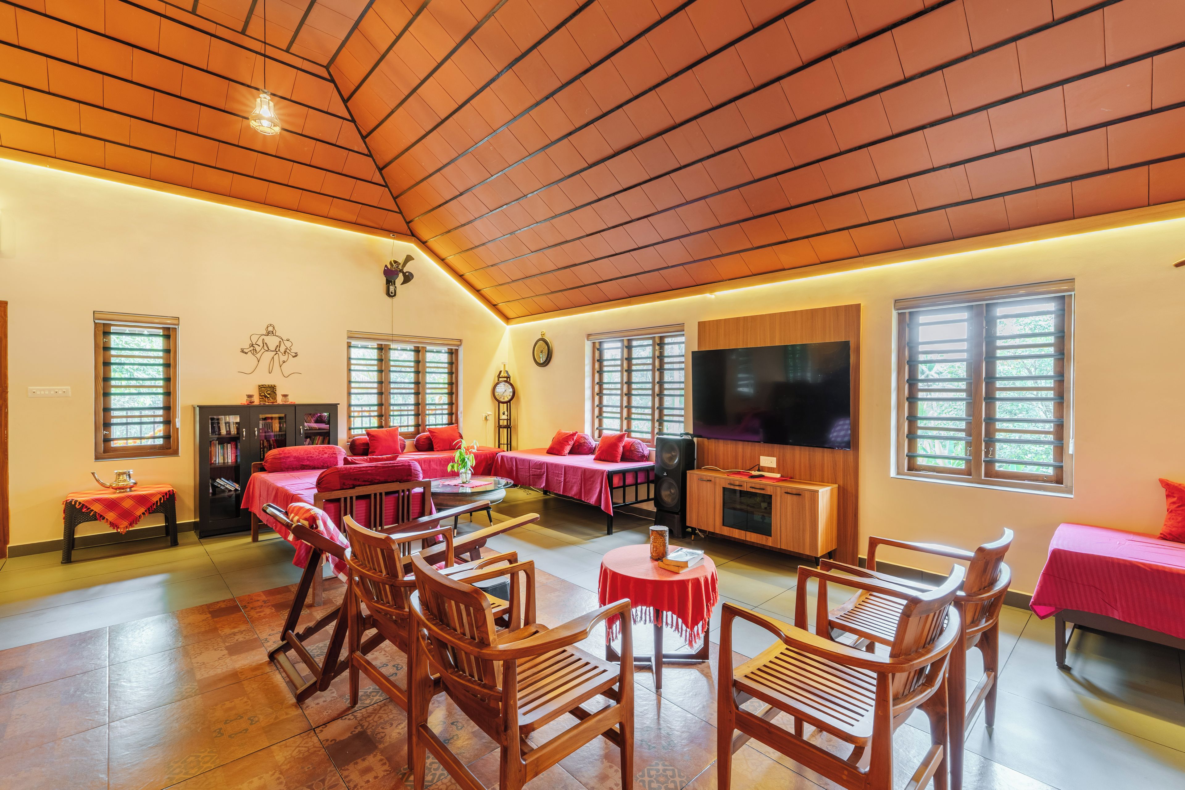 A spacious room with a high ceiling, wooden beams, a large flat-screen TV, multiple seating areas, and a bookshelf.