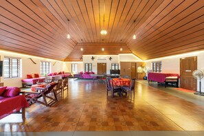 Un salón amplio con techos altos de madera y suelo a cuadros, con varias zonas de estar con mesas y sillas.