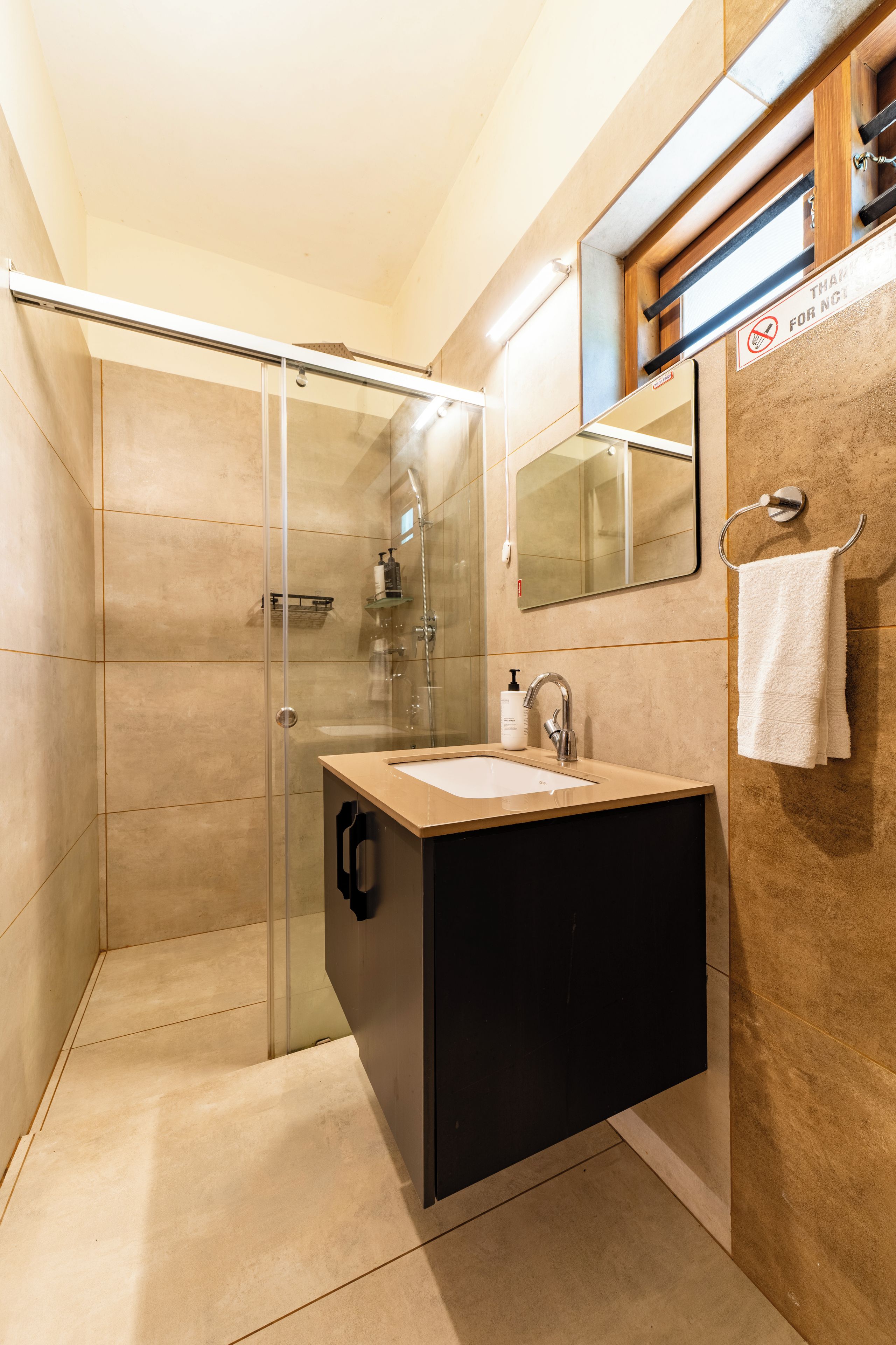 Un baño moderno con ducha envuelta en vidrio, tocador negro y espejo sobre el lavabo.