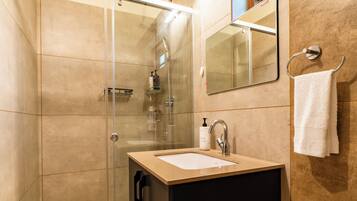 Un baño moderno con ducha envuelta en vidrio, tocador negro y espejo sobre el lavabo.