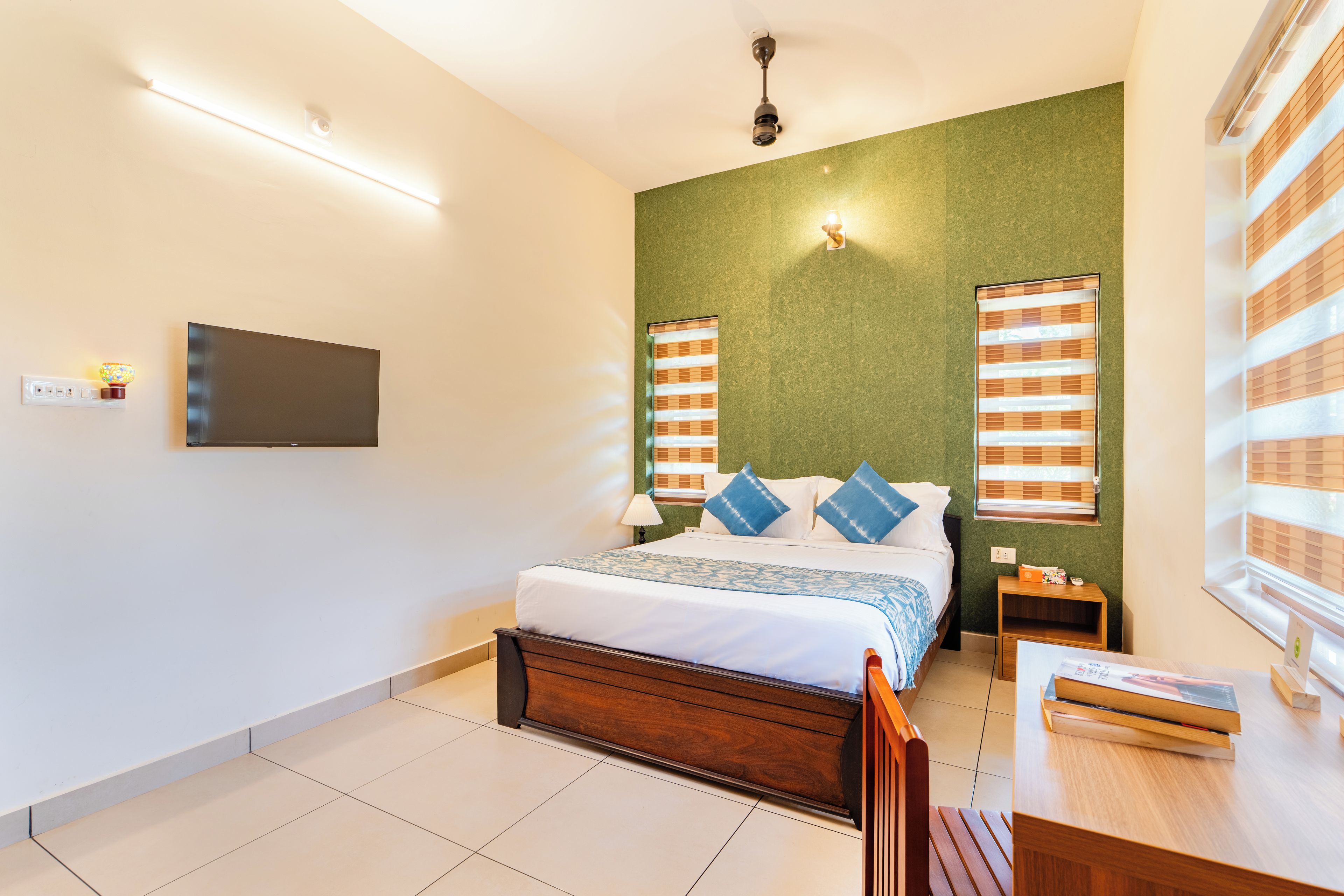 A hotel room with a bed, bedside table, lamp, and a television on the wall.