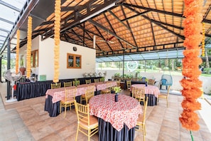 An outdoor covered dining area with multiple tables and chairs, a ceiling fan, and a view of greenery outside. - ELIVAAS Signature Pochans Zen 3BHK Villa (Thattekad)