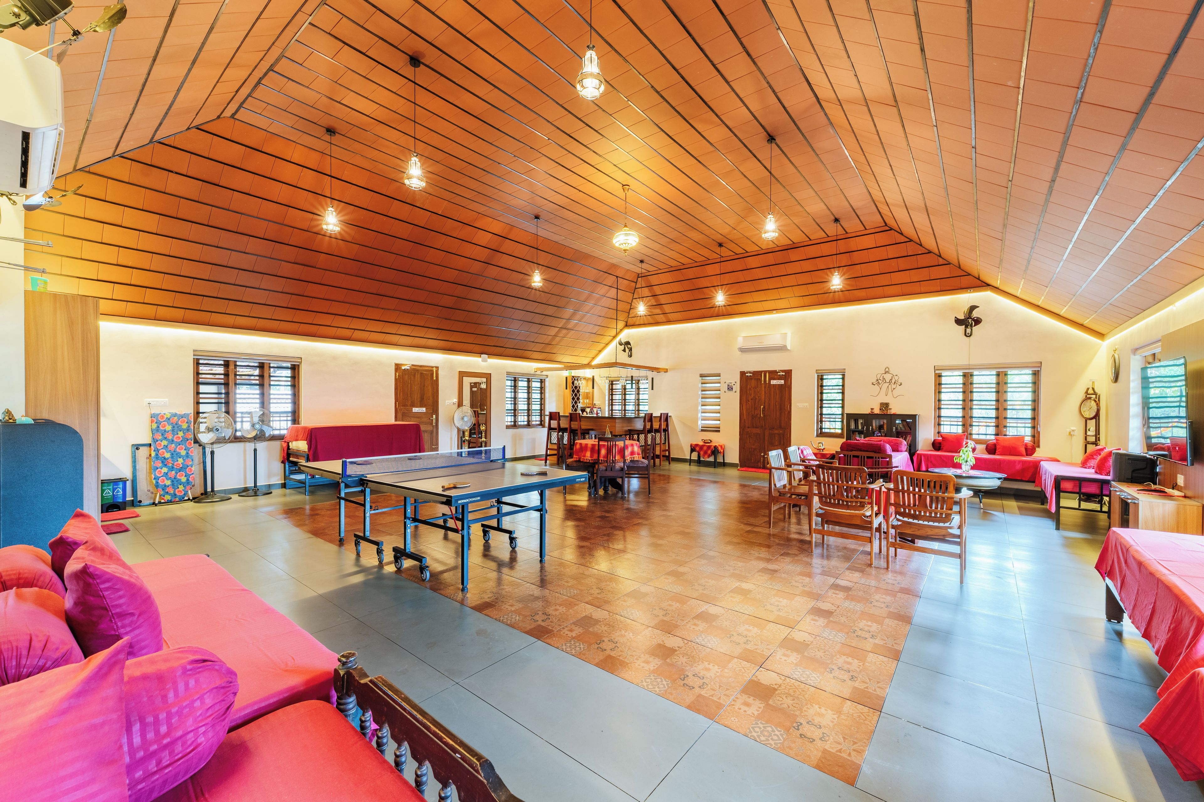 A spacious indoor area with a ping pong table, seating arrangements, and a high wooden ceiling.