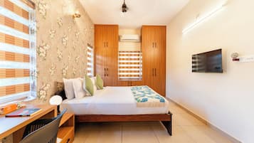 Un dormitorio con una cama, un escritorio con silla, un televisor y armarios de madera.