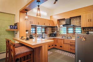 A kitchen with wooden cabinets, a central island, bar stools, a refrigerator, and a microwave. - ELIVAAS Signature Pochans Zen 3BHK Villa (Thattekad)