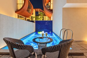 A pool area with two wicker chairs, a round table, and a glass of champagne.