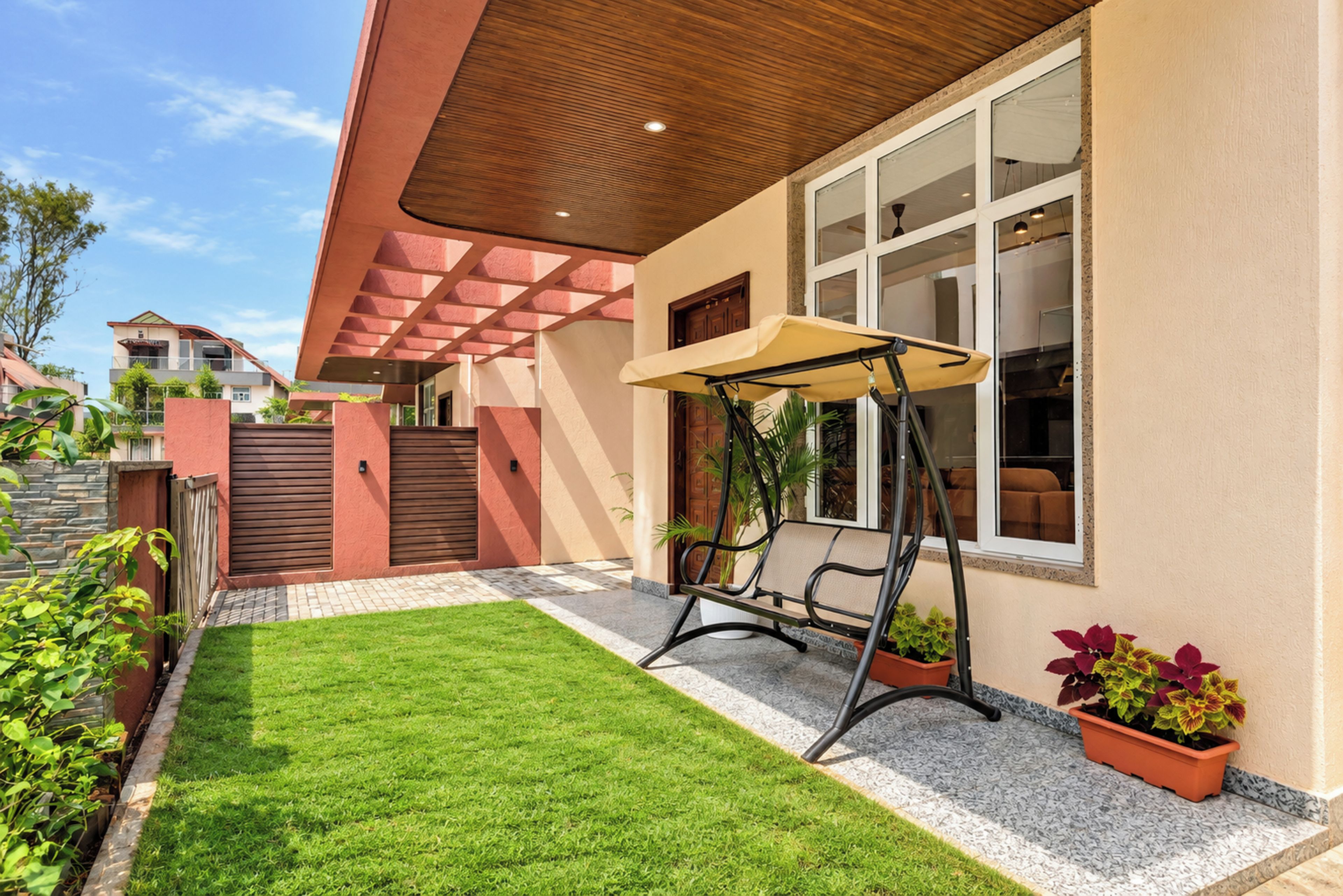 Una casa moderna con un prato curato, altalene e una zona patio con piante in vaso.