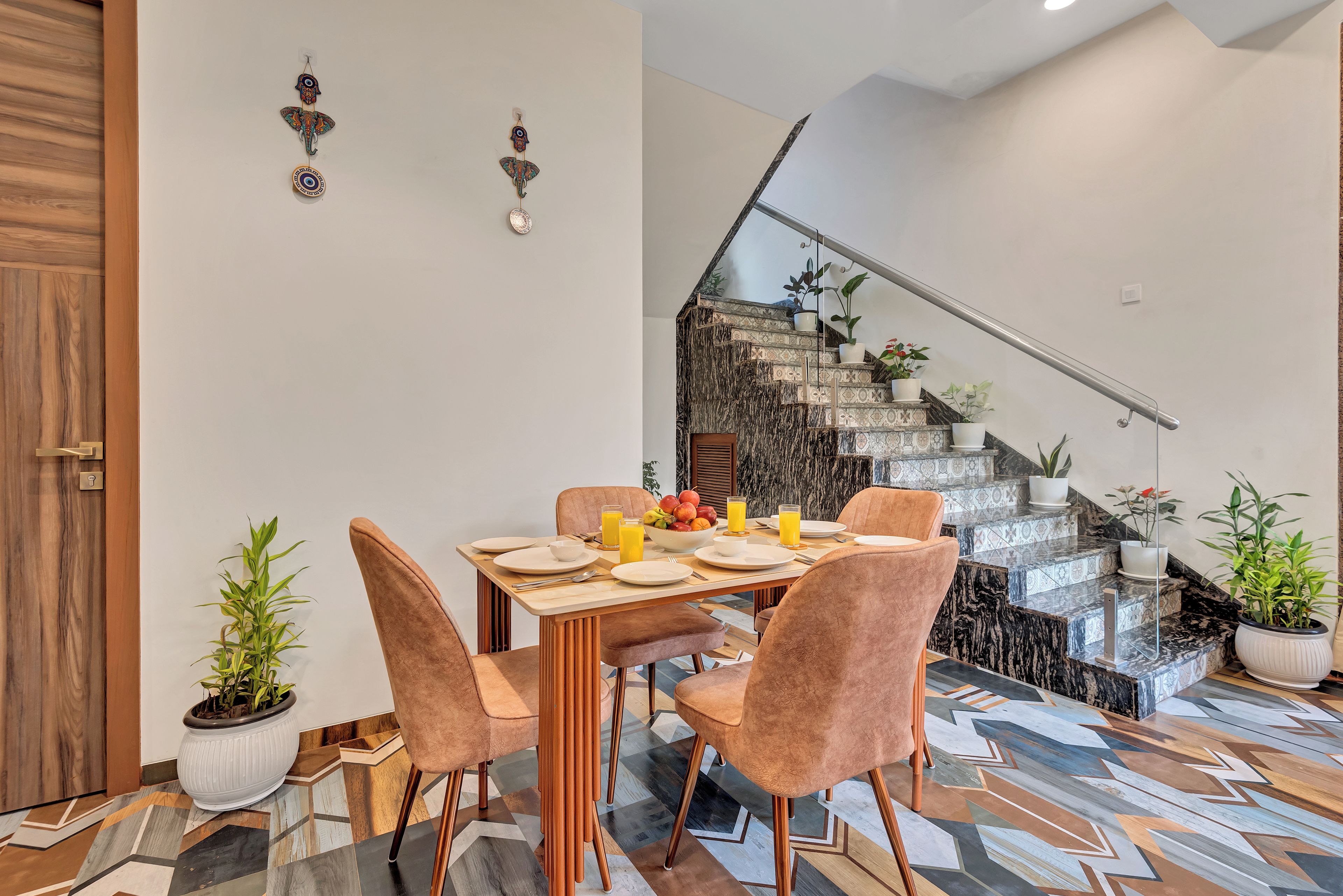 A dining area with a table set for four, a staircase with a railing, and potted plants.