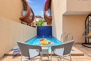 A poolside area with two wicker chairs, a table with fruit and drinks, and a blue-tiled pool. - ELIVAAS Signature Begonia Paradise 3BHK (Varsoli)