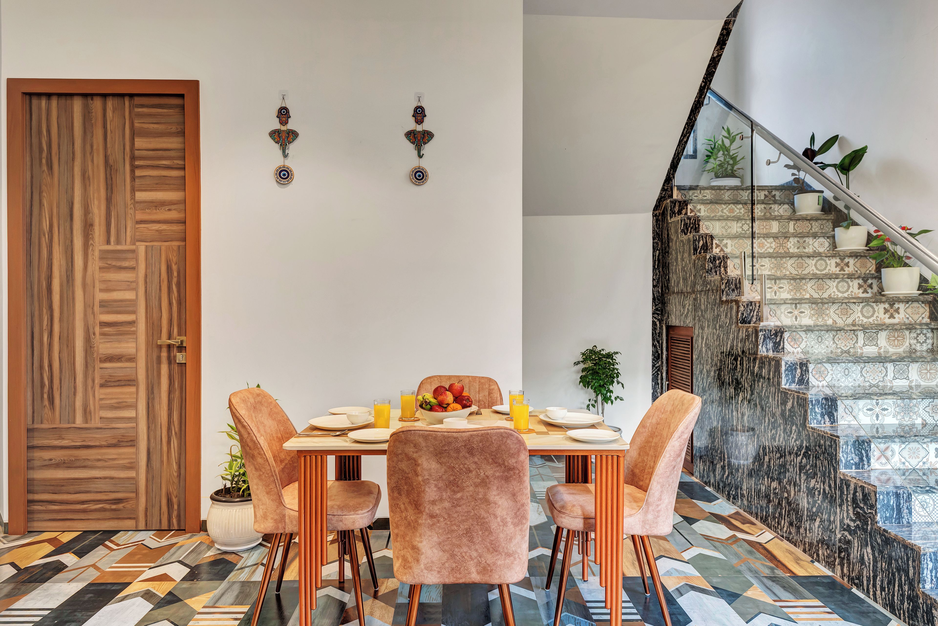 Zona pranzo con una porta in legno, una scala con piastrelle decorate e un tavolo apparecchiato con piatti, ciotole e frutta.