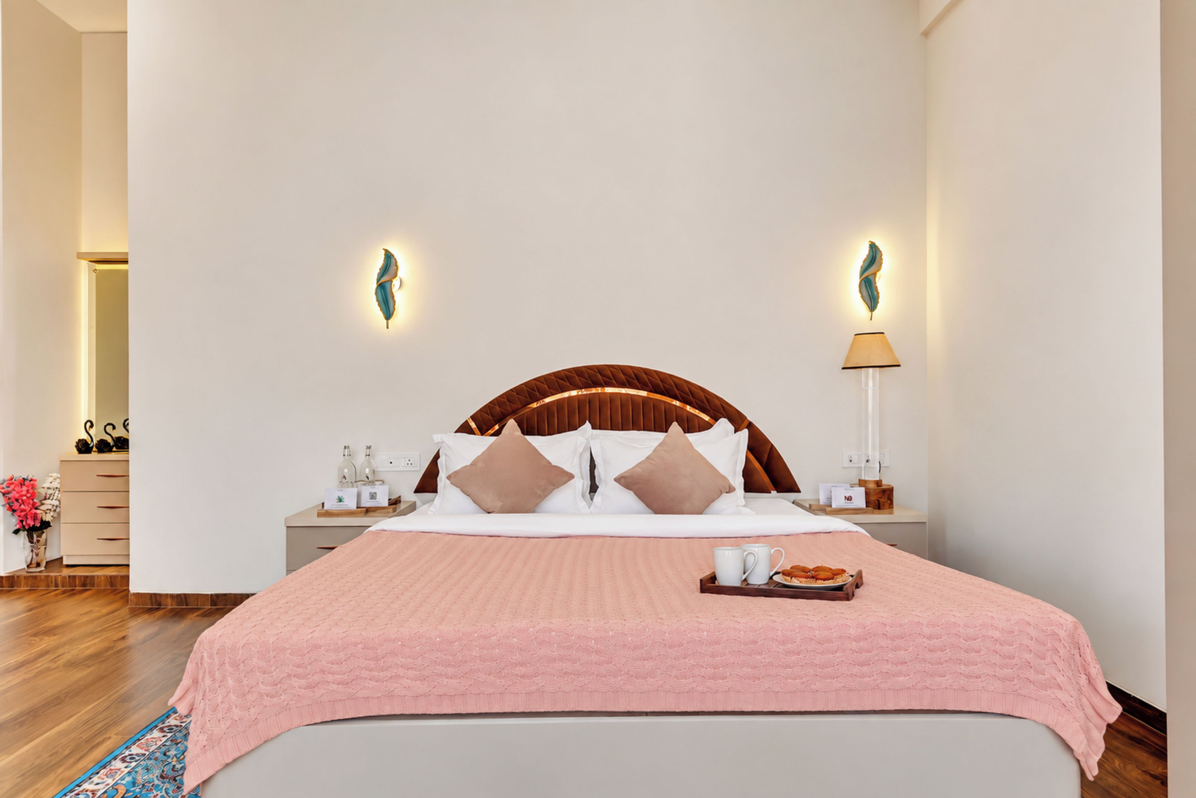A hotel room with a large bed, a wooden headboard, two bedside tables with lamps, and a pink bedspread.