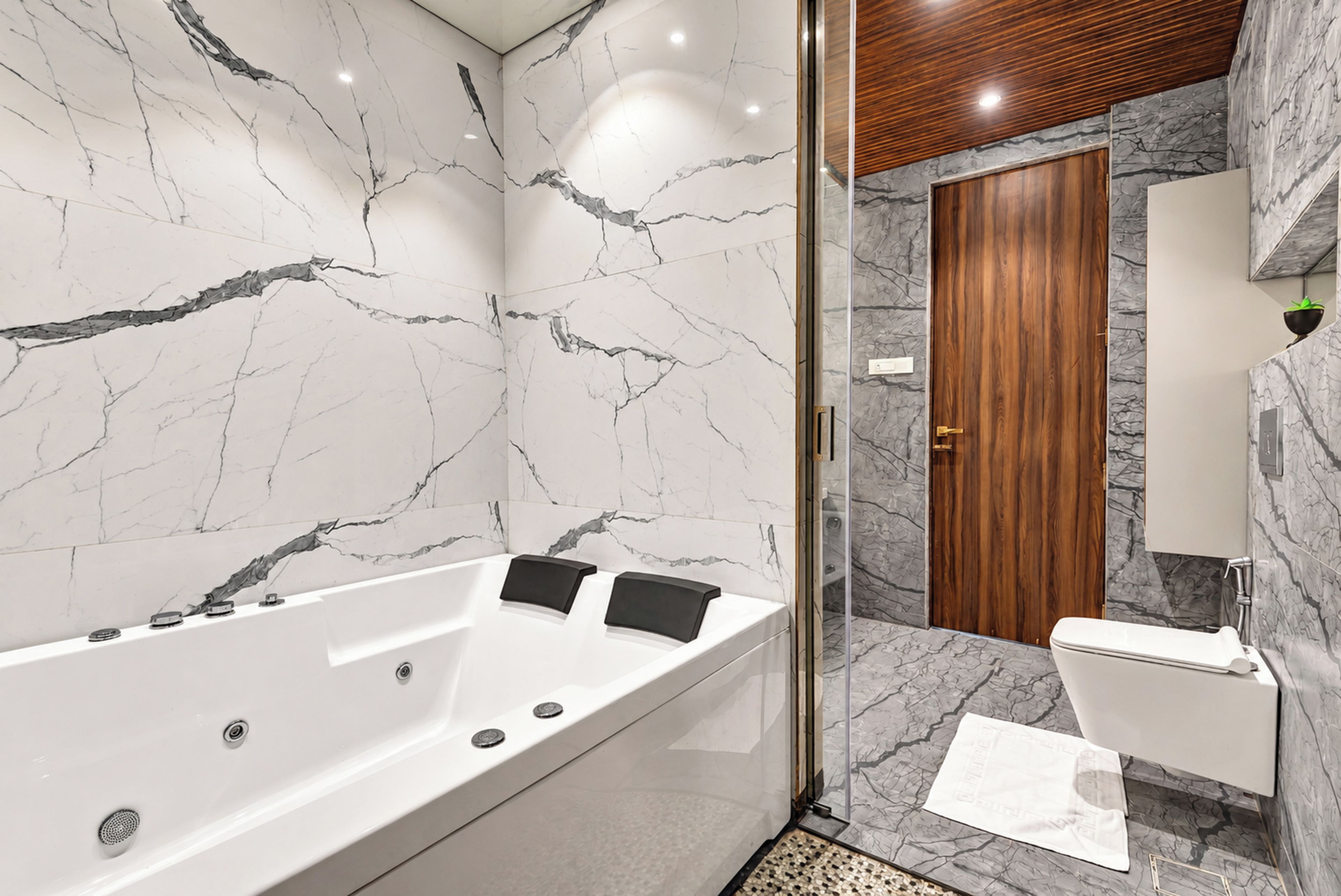 A modern bathroom with a marble wall, a freestanding bathtub, a wooden door, and a white sink.