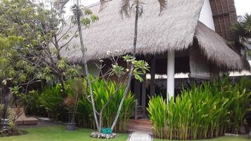 A thatched-roof structure with a pathway leading to it, surrounded by lush greenery and a small water feature.