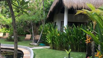 A tropical garden with a thatched-roof structure, a circular water feature, and various tropical plants.