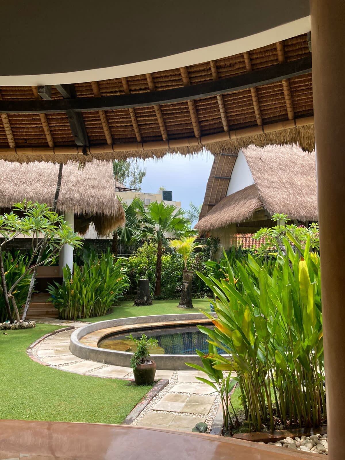 A tropical garden with a pool, thatched-roof structures, and lush greenery.