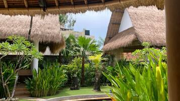 A tropical garden with a pool, thatched-roof structures, and lush greenery.