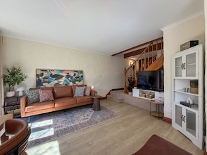 A living room with a sofa, a television, a bookshelf, and a staircase. - Dimora Court City Retreat (Adelaide)