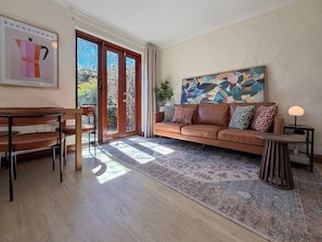 Ein modernes Wohnzimmer mit einem braunen Ledersofa, einem Couchtisch, einem Esstisch mit Stühlen und einem großen abstrakten Gemälde an der Wand.
