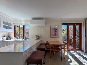 Eine moderne Küche mit einer zentralen Kochinsel, einem Essbereich mit Holzkästen und einem großen Fenster mit Blick auf Bäume.