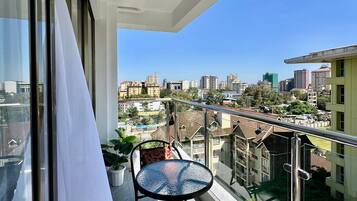 A balcony with a table and chairs, a white curtain, and a city view.