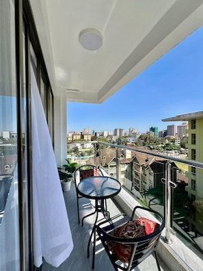 A balcony with a table and chairs, a white curtain, and a city view.