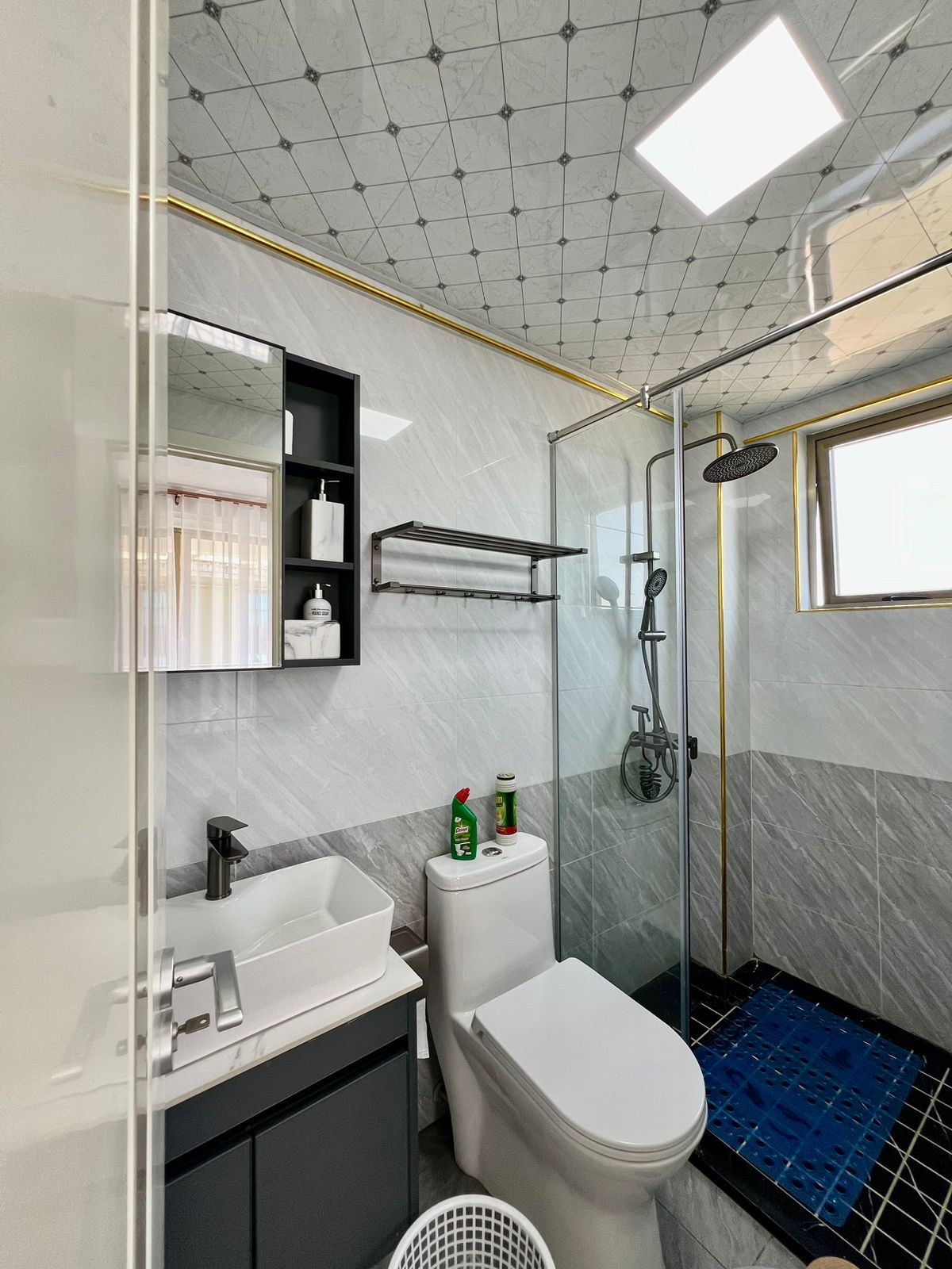 A modern bathroom with a glass shower enclosure, a white toilet, a sink with a mirror, and a shelf with toiletries.