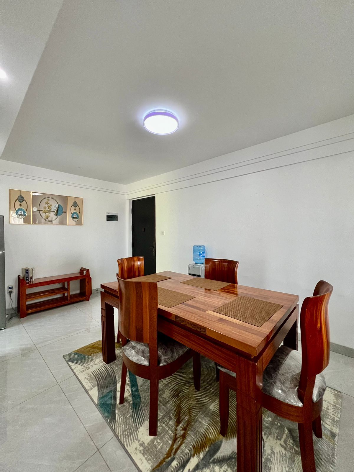Un comedor con una mesa y sillas de madera, un dispensador de agua y un banco.