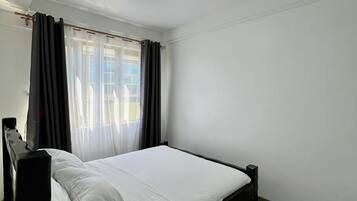 A bedroom with a bed, curtains, a ceiling light, and a furry rug.