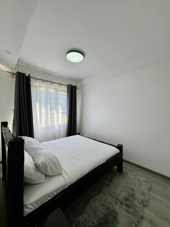 A bedroom with a bed, curtains, a ceiling light, and a furry rug.