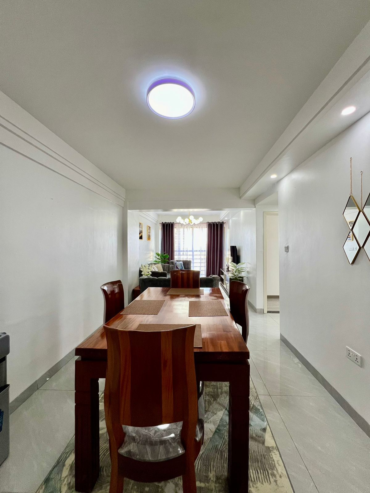 Un espace repas avec une longue table en bois, des chaises et un luminaire moderne au plafond.