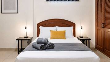 A neatly made bed with white and gray linens, a wooden headboard, and two bedside lamps.