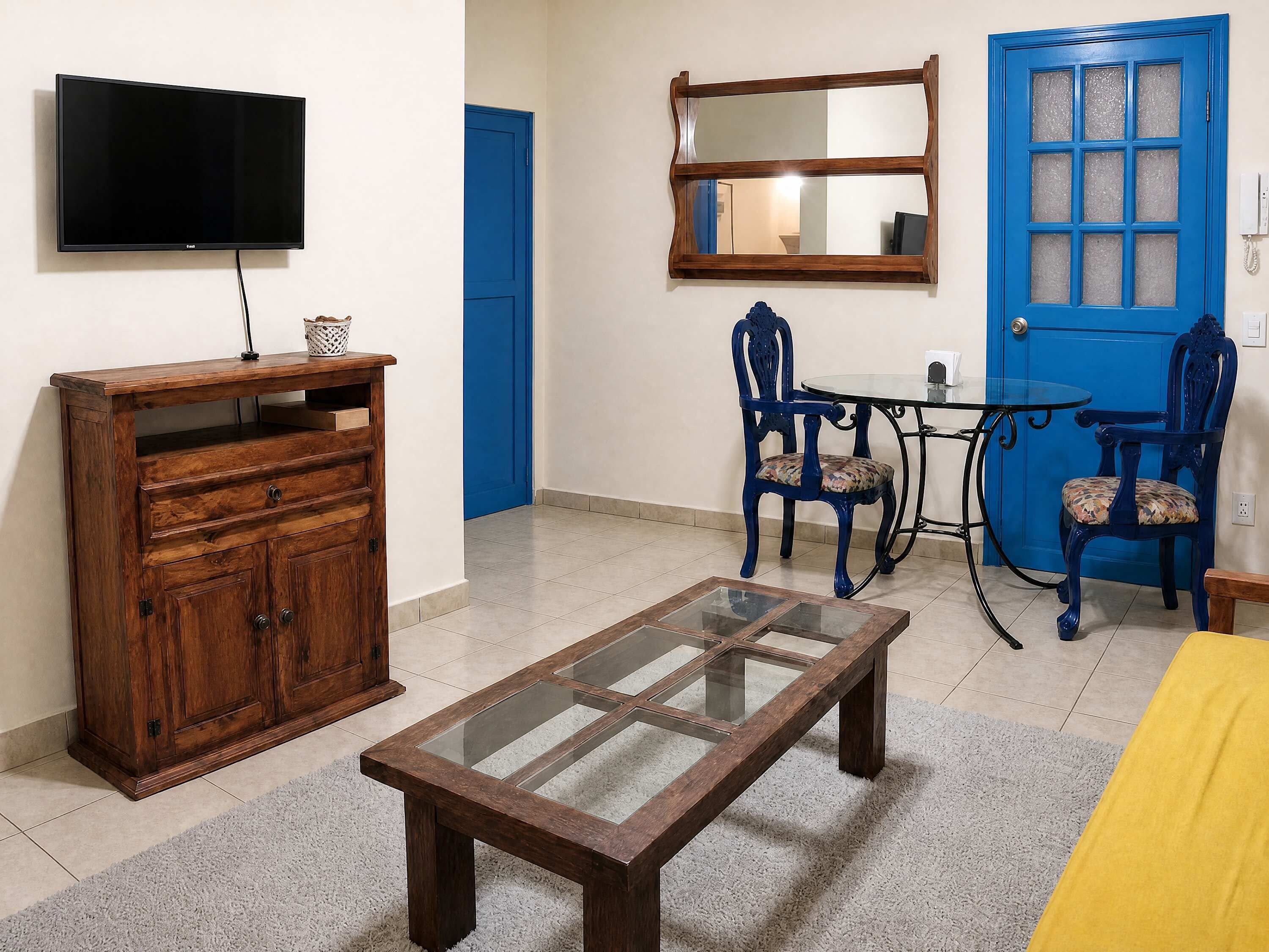 A living room with a TV, wooden cabinet, glass coffee table, blue chairs, and a blue door.