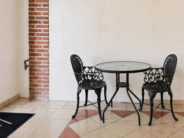 A small round table with two chairs, a brick wall, and a tiled floor.