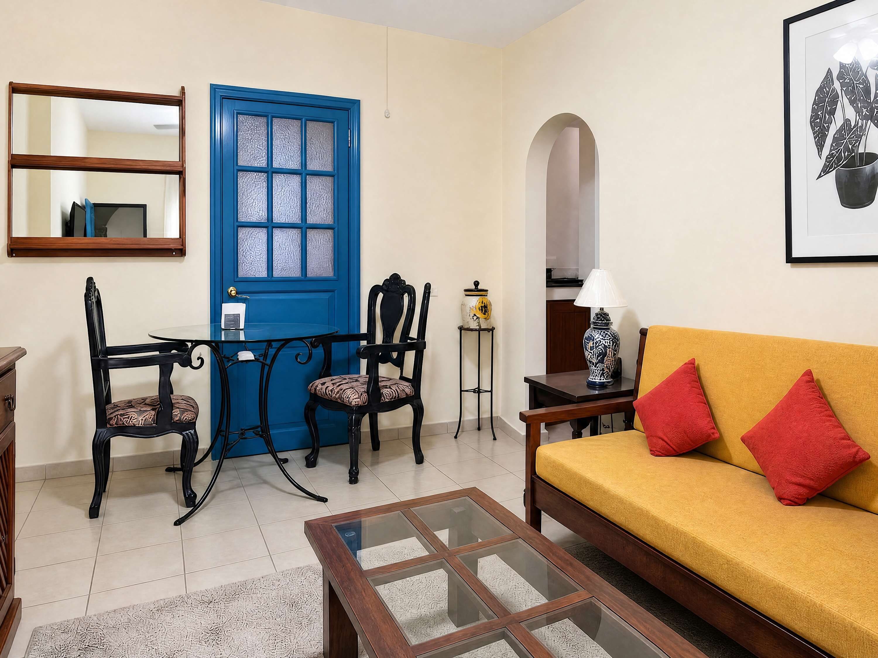 A living room with a blue door, a sofa with red cushions, a coffee table, and a chair with a patterned cushion.