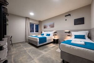 Habitación de hotel con dos camas, un escritorio, una silla, un ventanal con cortinas y un cuadro en la pared.