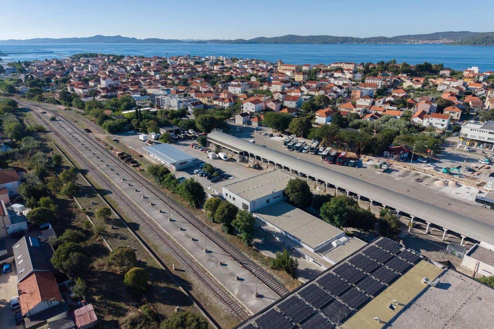 An aerial view of a coastal town with a railway station, a parking lot, and solar panels.