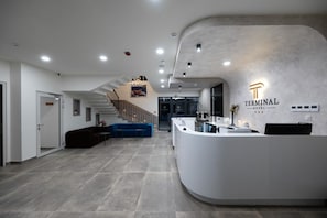 Un hall d’hôtel moderne avec un comptoir d’accueil incurvé, un escalier et un canapé bleu.
