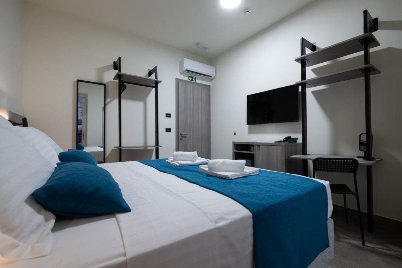 Una habitación de hotel con una cama, un escritorio, una silla, un televisor y un equipo de aire acondicionado.