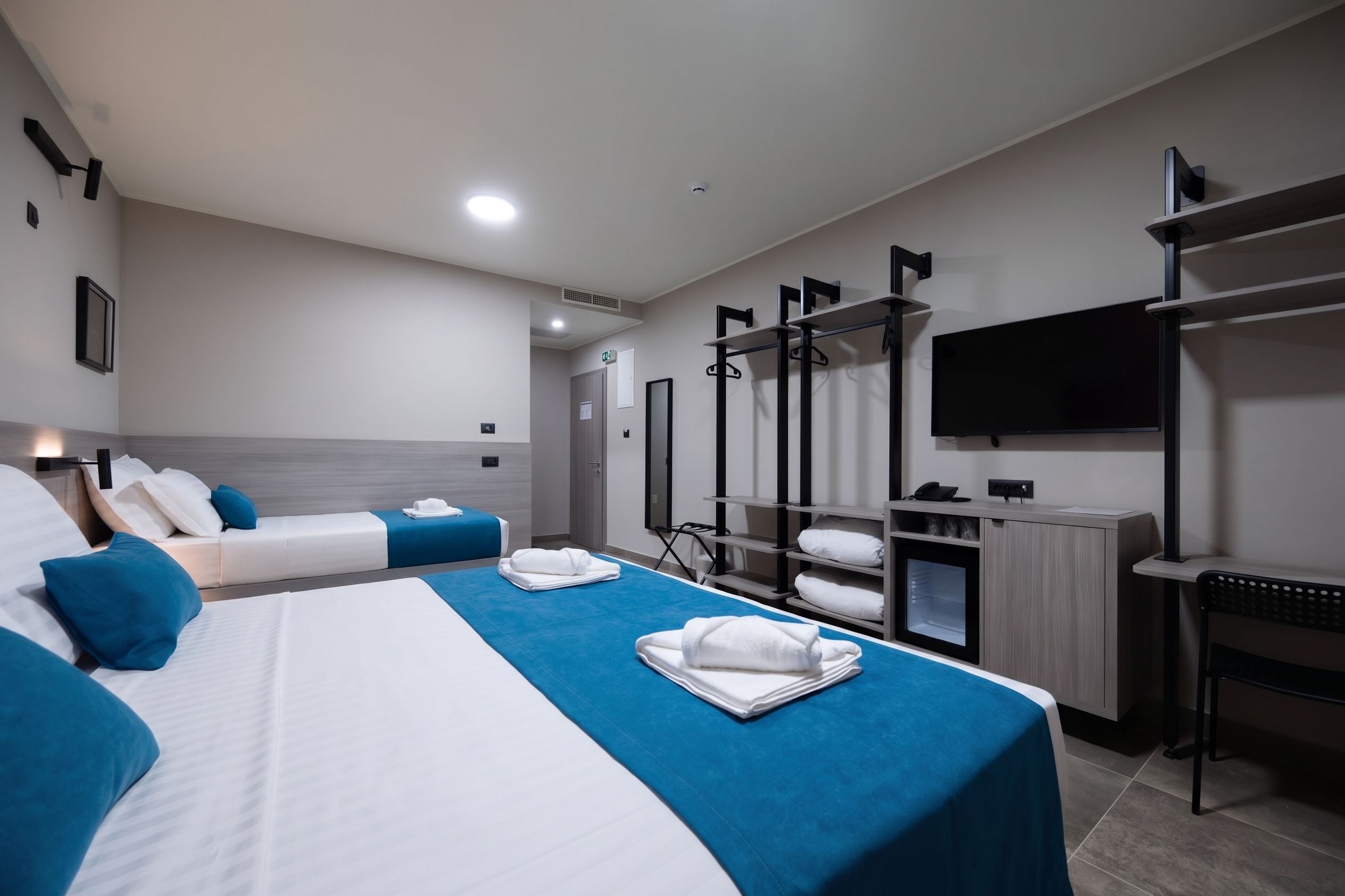 Een hotelkamer met twee bedden, een bureau, een televisie en een kledingkast.