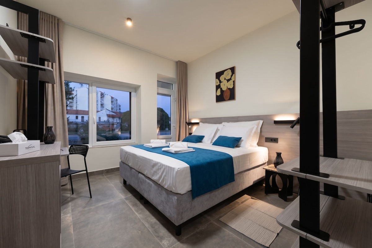 Une chambre d’hôtel moderne, dotée d’un grand lit, d’un bureau et d’une fenêtre donnant sur des immeubles.