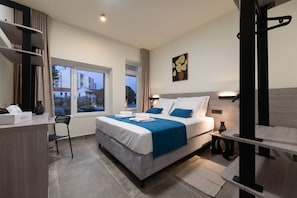 Une chambre d’hôtel moderne, dotée d’un grand lit, d’un bureau et d’une fenêtre donnant sur des immeubles.