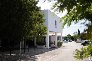 Un edificio moderno con fachada plana, un acceso cubierto y un estacionamiento con automóviles.