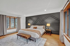 Primary Bedroom offers a king bed, TV, and peaceful forest views for a restful escape. - Big Bass Lake • Shared Pool + Fire Pit + Game Room | Lake House Retreat (Big Bass Lake)