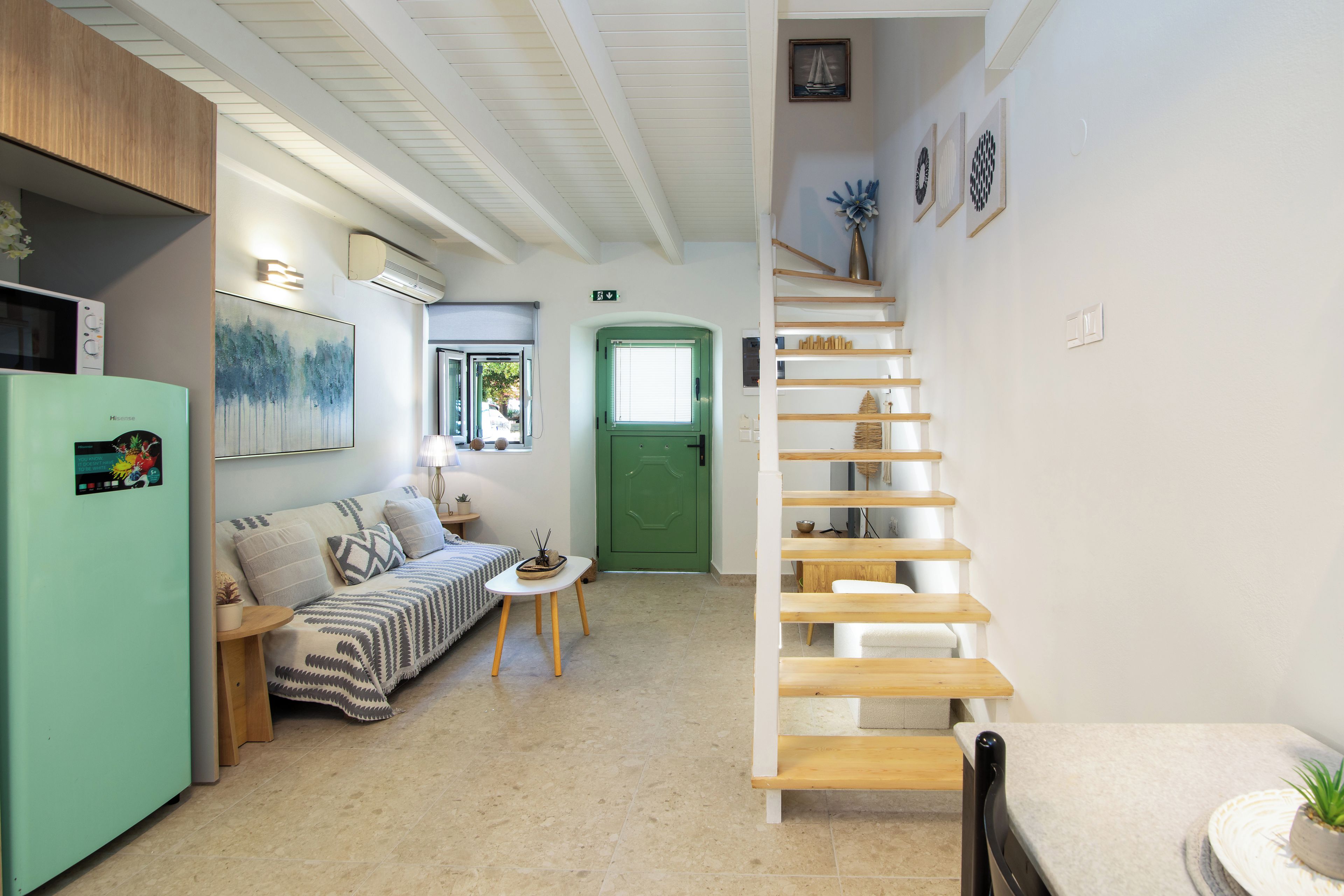 A modern interior with a sofa, a dining table, a staircase, and a green door.