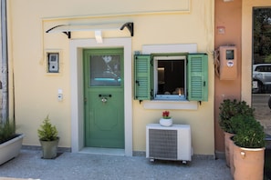 Un bâtiment avec une porte verte, une fenêtre avec des volets verts et un appareil de climatisation.